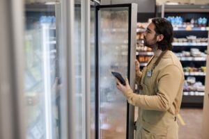 Male worker in supermarket inspecting freezer