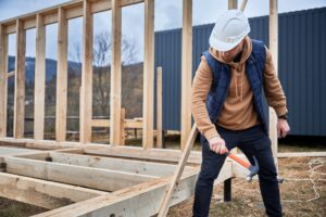 Man worker hammering while building wooden frame house.