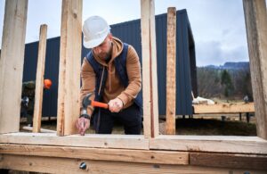 Man worker hammering while building wooden frame house.