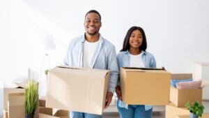Relocation concept. Happy african american couple carrying cardboard boxes into new house, smiling