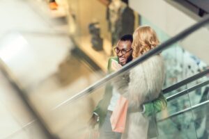 stylish young couple riding escalator and embracing at shopping mall
