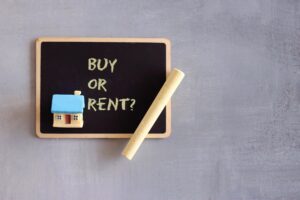 Top view of chalkboard with text BUY OR RENT, toy house and chalk
