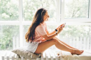 woman in pink t-shirt with cup of coffee surfs internet with modern mobile phone